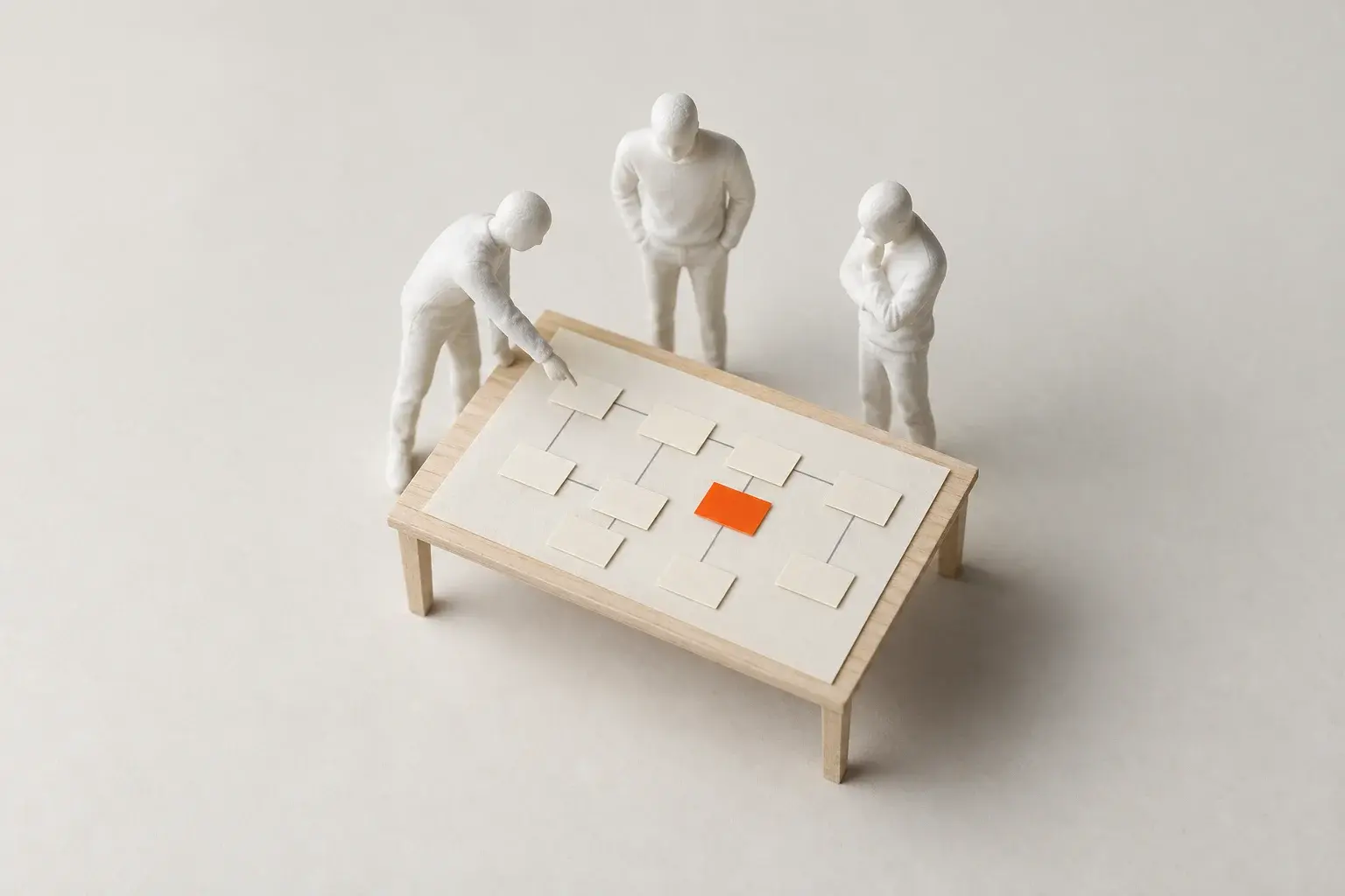 A paper model of three figures around a table, pointing at a process map made of small cards.